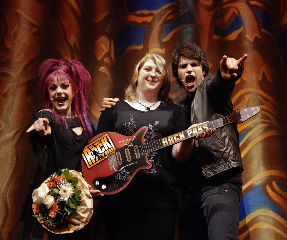 Überreichten eine Gitarre: die Darsteller Jessica Kessler l.) und Sascha Alexa mit der 500.000. Besucherin von "We Will Rock You"