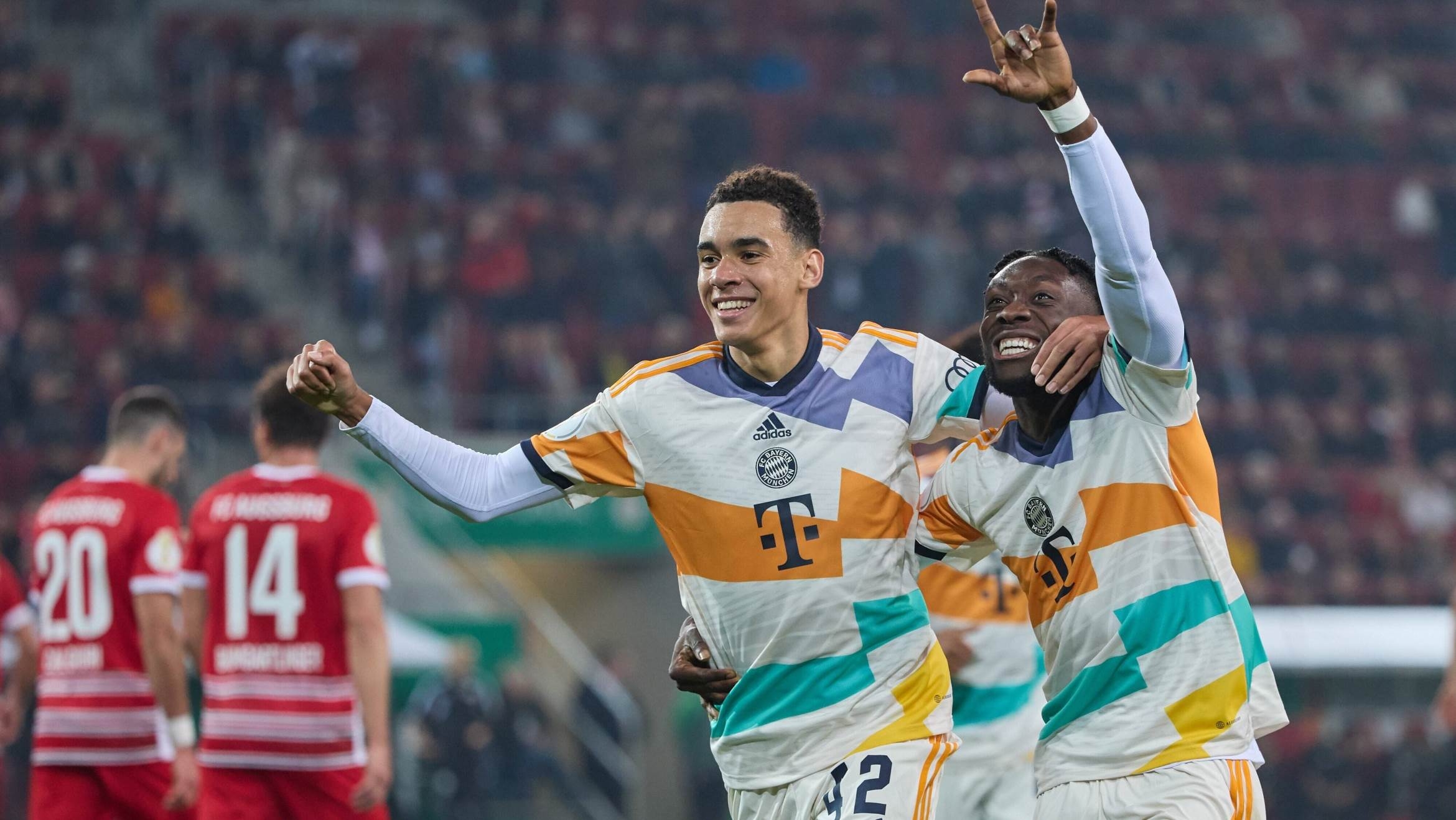 Jamal Musiala (l.) und Alphonso Davies jubeln über ein Tor gegen den FC Augsburg - 