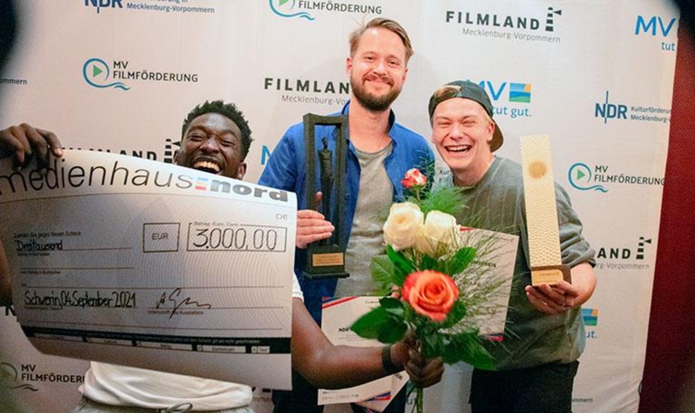 Die Hauptdarsteller Farba Dieng (li.) und Julius Nitschkoff (re) freuen sich mit Regisseur Florian Dietrich (Bildmitte) über die Auszeichnungen für "Toubab" beim Filmkunstfest MV 